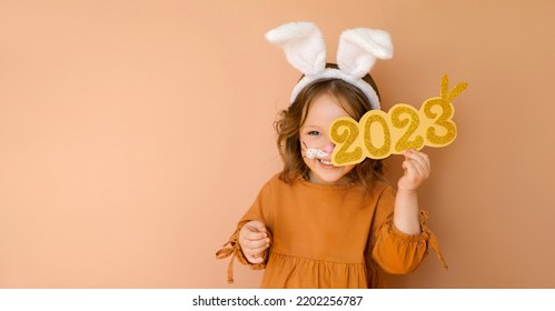 A funny laughing child in the guise of a rabbit closes his eye with the numbers 2023. The year according to the zodiac sign of the Eastern calendar. Christmas Greeting poster - Shutterstock ID 2202256787