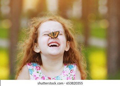 Lächelndes, lockiges Mädchen mit einem Schmetterling auf der Nase. Gesundes Lächeln mit weißen Zähnen. Kostenloses Atemkonzept.