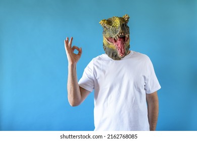 Funny laughing dinosaur head on human body on white t-shirt on blue background, with hand signal ok . Clip art, negative space.