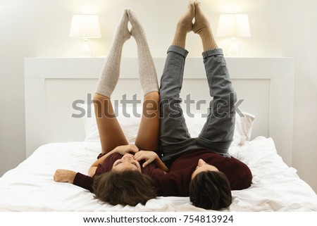 Funny and lazy couple is lying on the bed with legs up