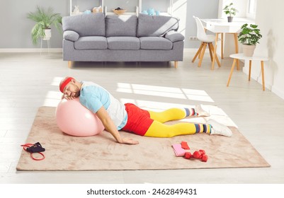 Funny lazy tired man takes a nap while working out. Weak weary young man in retro sports clothes and headband resting his head on yoga ball while sleeping on floor in living room after fitness workout - Powered by Shutterstock