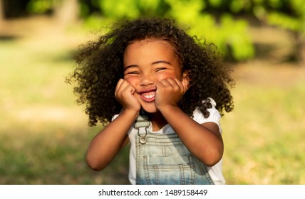 Funny little afro girl touching cheeks and having fun in nature park