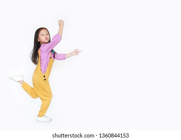 Funny Little Asian Child Girl In Pink-yellow Dungarees Jumping Over White Background With Copy Space. Freedom Kid Movement Concept.