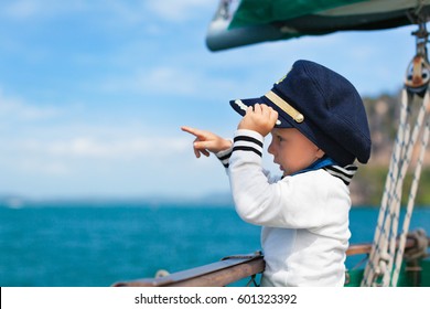 Funny little baby captain on board of sailing yacht watching offshore sea on summer cruise. Travel adventure, yachting with child on family vacation. Kid clothing in sailor style, nautical fashion.