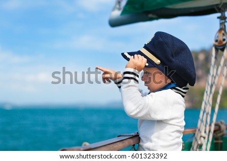 Funny little baby captain on board of sailing yacht watching offshore sea on summer cruise. Travel adventure, yachting with child on family vacation. Kid clothing in sailor style, nautical fashion.
