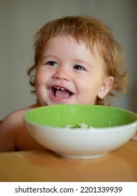 Funny Little Baby In The Kitchen Eating With Fingers From Plate. Fun Child Face Closeup.