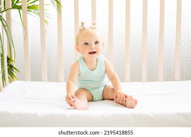 Funny little baby standing in a crib in a white nursery with a window. A little girl in a cotton bodysuit. Smiling blue-eyed baby - Powered by Shutterstock