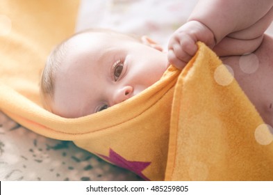 Funny Little Baby Wearing A Diaper Playing On Bed In Nursery Room. Happy Child After Bath Or Shower. Infant Kid Diaper Change And Skin Care. Smiling Kid Playing With His Feet.