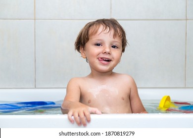 Funny Little Boy Getting A Bath In The Bathroom, He Has A Naughty Face. 2 Years Child Bathes In Bathtub With Toys In The Water.