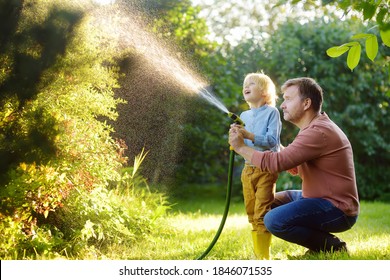 Funny little boy with his father watering plants and playing with garden hose in sunny backyard. Preschooler child having fun with spray of water. Summer outdoors activity for kids.