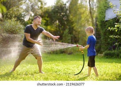 Funny little boy with his father playing with garden hose in sunny backyard. Preschooler child having fun with spray of water. Summer outdoors activity for family with kids. - Powered by Shutterstock