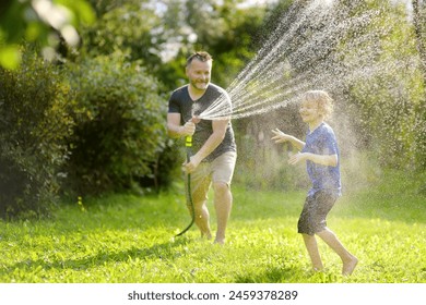 Funny little boy with his father playing with garden hose in sunny backyard. Preschooler child having fun with spray of water. Summer vacation in the village for family with kids. - Powered by Shutterstock