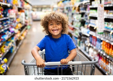 Funny little boy laughing while sitting in a shopping cart during a family trip to the grocery store. He is excited to buy something new - Shutterstock ID 2171562923