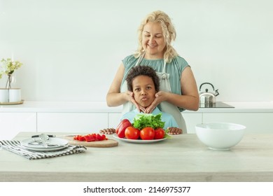 Funny Little Child With Black Hair And Mother In Kitchen At Home. 