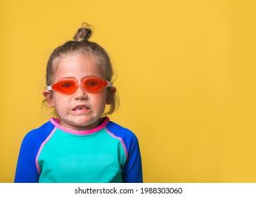 Funny Little Child Girl In Swimsuit, Swimming Goggles And Swim Cap Isolated On Yellow Background. Funny Portrait Of Small Kid Ready To Swim Or Dive In Swimming School Or Water Park. Emotional Diver