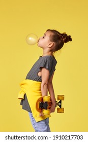 Funny Little Child Girl With Yellow Skateboard Blowing A Big Bubble Gum Over Yellow Background