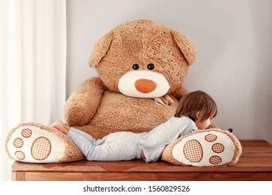 Funny Little Child In Pyjama Lying On Big Plush Puffy Teddy Bear Toy Watching Cartoons On Mobile Phone. Leisure Time. Cozy Home. Babysitting Concept