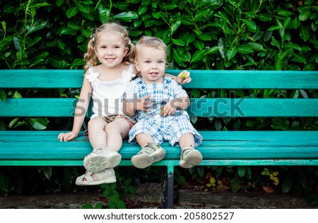 funny little children brother and sister sitting on bench