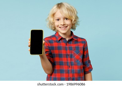 Funny Little Curly Kid Boy 13s Years Old In Basic Red Checkered Shirt Hold Mobile Cell Phone With Blank Empty Screen Isolated On Blue Background Children Studio Portrait. Childhood Lifestyle Concept