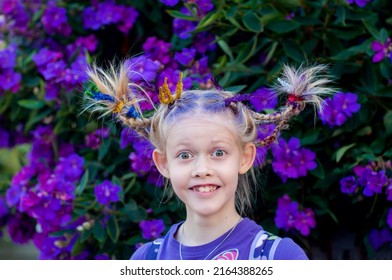 Funny little cute caucasian girl with braids for crazy hair day at school on purple flowers tibouchina outside nature background - Shutterstock ID 2164388265