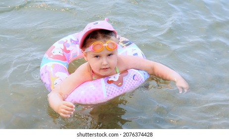 Funny Little Girl 3 Years Old Swims With An Inflatable Ring, A Sun Cap And Swimming Goggles In The Sea. Summer Vacation Concept, Learning To Swim: Antalya, Manavgat Turkey - July 28, 2021.