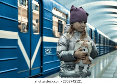 Funny little girl 5 year old posing on platform metro station. Kid girl passenger with plush toy in subway station in front of train, people city. Public urban transportation concept. Copy text space