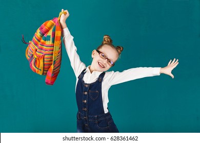 Kleines, lustiges Mädchen mit großem Rucksack springen und Spaß an der türkisfarbenen Wand haben. Schulkonzept.Zurück zur Schule. Die Schule ist im Sommer draußen. Abschluss eines weiteren erfolgreichen Schuljahres