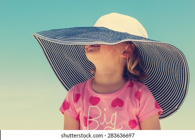 Funny Little Girl In A Big Striped Hat On The Beach. The Image Is Tinted.