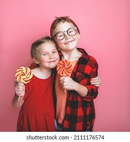 Funny Little Girl And Boy Holding Sugar Lollipop. Laughing Kids Eating Candy Isolated On Colorful Background. Delighted Kid Radiates Positive Emotions. School Children Lunch. Healthy Food.