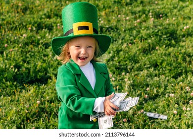 Funny little girl dressed as a leprechaun, he holds money in his hands and laughs. A child on a background of green clover. St. Patrick's Day Celebration space for text, copyspace