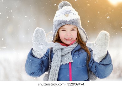 Funny little girl having fun in beautiful winter park during snowfall
