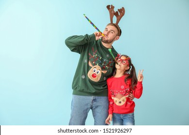 Funny Little Girl And Her Father In Christmas Sweaters And With Party Whistles On Color Background