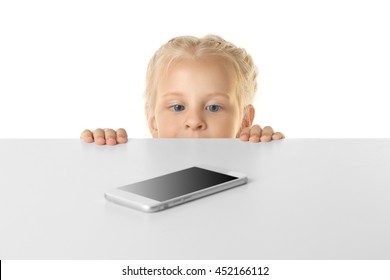 Funny Little Girl Hiding Behind White Table And Looking At Mobile Phone