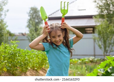 Funny Little Girl Holding Small Gardening Tools , Standing In The Garden