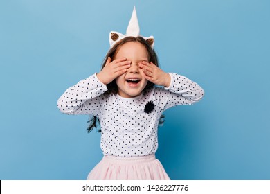 Funny little girl laughs with her eyes closed. Child in image of unicorn having fun on blue background