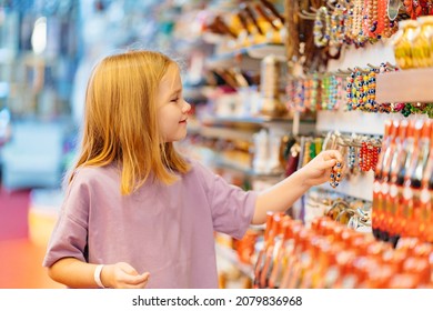 a funny little girl looks with interest at jewelry and souvenirs in the store. sale of goods in the hotel and by the beach in the resort.