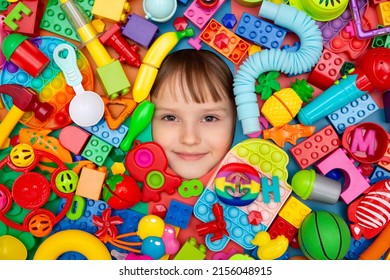 Funny little girl lying in the chaos of toys. A child's face surrounded by building blocks and toys.
