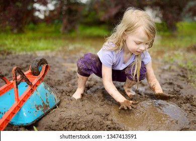Das sonnige kleine Mädchen spielt in einer großen Schlammpfütze am sonnigen Sommertag. Kinder werden schmutzig, während sie in schlammigem Boden graben. Gesunde Spiele im Freien.