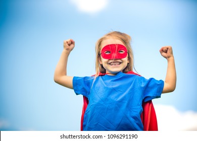 Funny little girl playing power super hero over blue sky background. Superhero concept. - Shutterstock ID 1096291190
