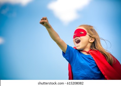 Funny little girl playing power super hero over blue sky background. Superhero concept. - Powered by Shutterstock