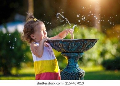 A Funny Little Girl Is Playing With The Spray Of A Drinking Water Fountain In The Park. Childhood, Child, Summer Time, Heat. Solar Protection For Children's Skin,