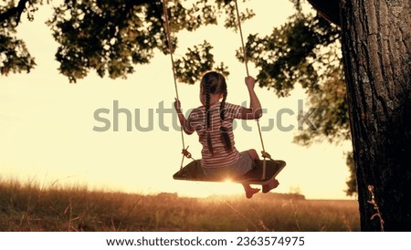 Funny little girl plays swings under old tree at sunset time. Happy little girl enjoys flight feeling on swings in country field on summer holiday. Little girl rides handmade swing in country garden Stock photo © 