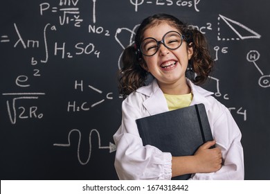funny little girl science student in lab coat laughing with a notebook on school blackboard background with science formulas, back to school and successful female career concept - Shutterstock ID 1674318442