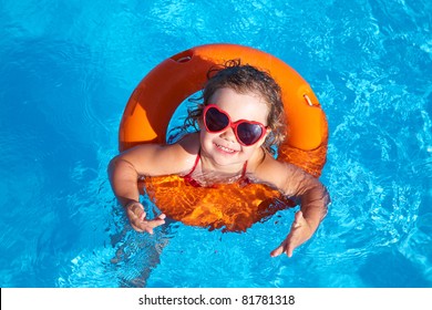 Funny Little Girl Swims In A Pool In An Orange Life Preserver