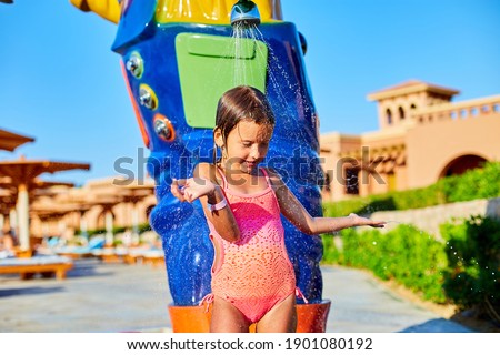 Funny little girl in swimsuit cooling in shower outside, child play with water in resort near swim pool, summer time, vacation.