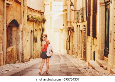 Funny Little Girl Traveler Walking On The Streets Of Provence, Wearing Backpack. Travel With Kids, Family Vacation On South Of France, Image Taken In Montpellier