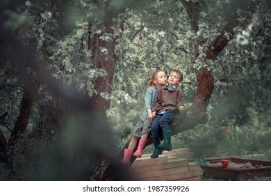 Funny Little Girl Is Trying To Kiss Little Boy Sitting Near Her On The Blossoming Apple Tree. The Boy Doesn't Want To Be Kissed And Makes A Funny Face Expression. Image With Selective Focus And Toning