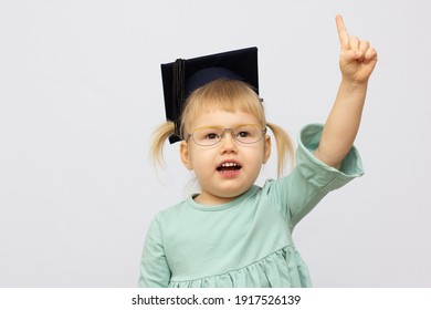 Funny little girl wearing eyeglasses imitates a teacher against white background. Little student put finger up Looking at camera. School concept. Back to School