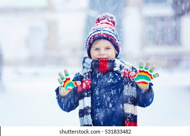 Funny Little Kid Boy In Colorful Clothes Playing Outdoors During Snowfall. Active Leisure With Children In Winter On Cold Snowy Days. Happy Child Having Fun And Playing With Snow