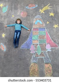Funny little kid boy flying in universe by space shuttle picture painting and colorful chalks  Creative leisure for children outdoors in summer 